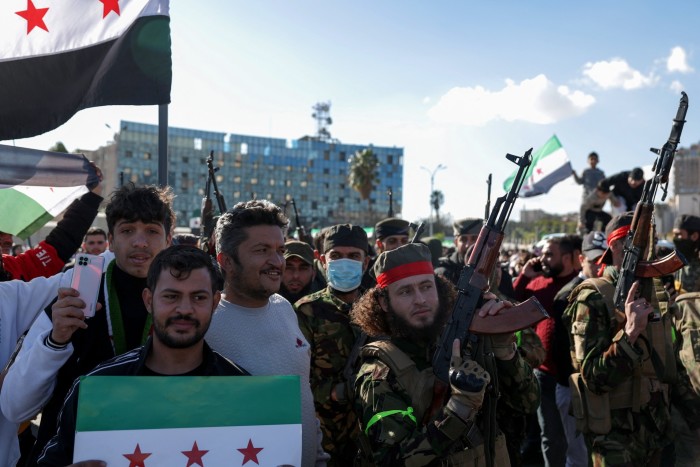 Rebeldes armados se unen a una gran multitud de sirios que ondean banderas de la época de la independencia, utilizadas por la oposición desde que comenzó el levantamiento en 2011, durante las celebraciones tras el derrocamiento de Assad en la céntrica plaza Omeya de Damasco el viernes.