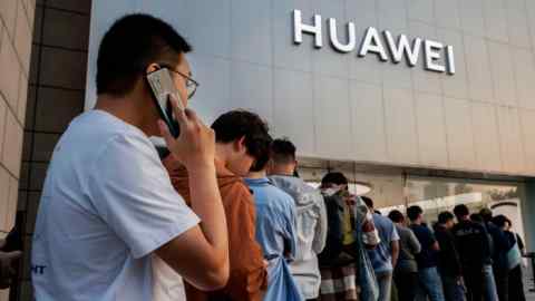 La gente hace cola frente a una tienda insignia de Huawei en Beijing, China. Un hombre en primer plano habla por un teléfono móvil Huawei.