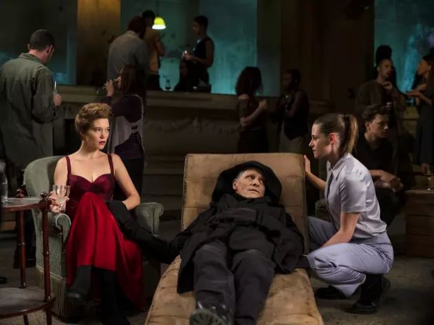 Escena de crímenes del futuro que muestra a un hombre acostado en un salón de chaise mientras dos mujeres lo atienden.