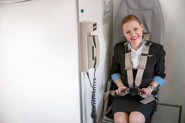 Mujer Joyful Woman Air Anfante de aire mirando la cámara y sonriendo mientras está sentada cerca del teléfono en la cabina de la aeronave