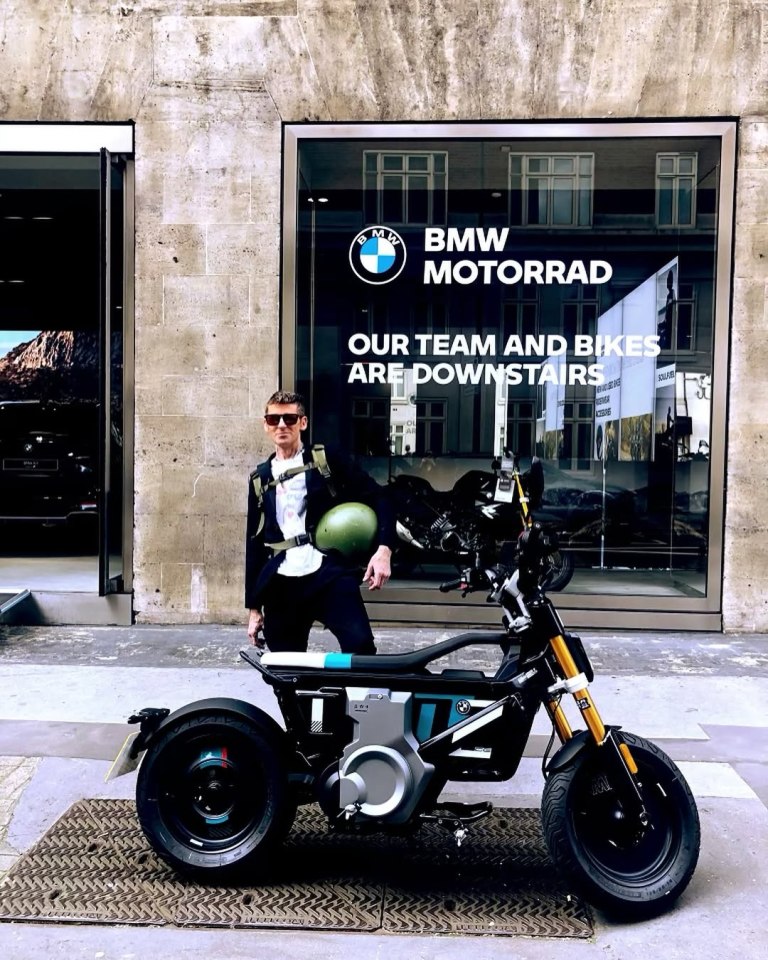 Hombre de pie junto a una motocicleta BMW eléctrica fuera de una tienda BMW Motorrad.