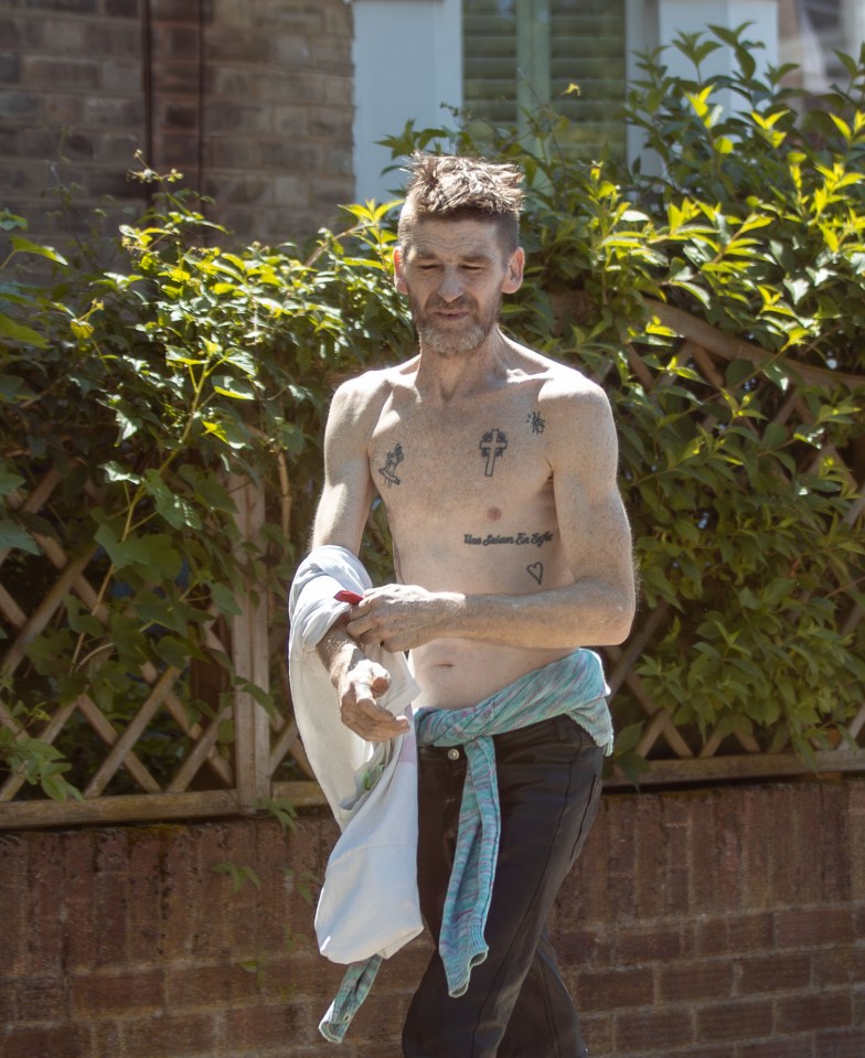 Un hombre tatuado caminando por la calle, sosteniendo una camisa.
