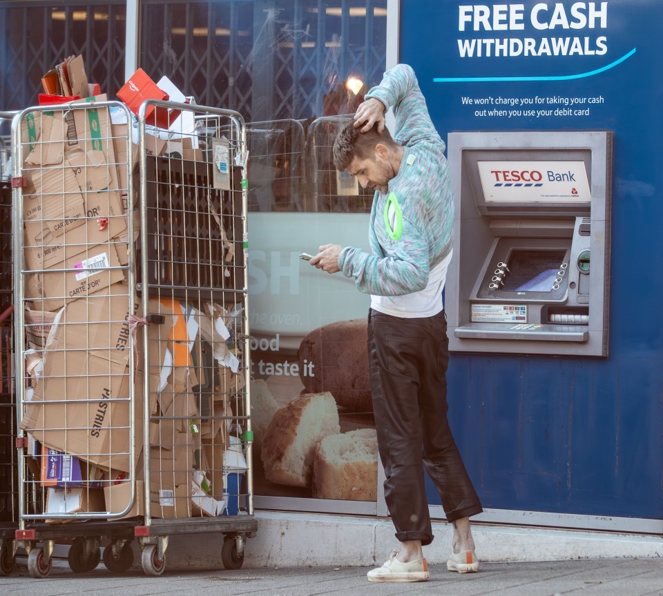 Hombre usando el teléfono en el cajero automático, reciclaje de contenedor cercano.