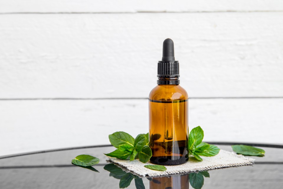 Botella ámbar de aceite esencial de menta con hojas de menta fresca.