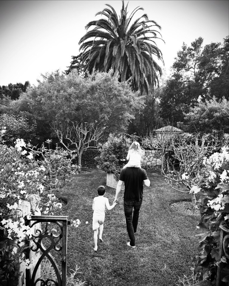 Foto en blanco y negro de Meghan, Harry y sus hijos caminando en un jardín.