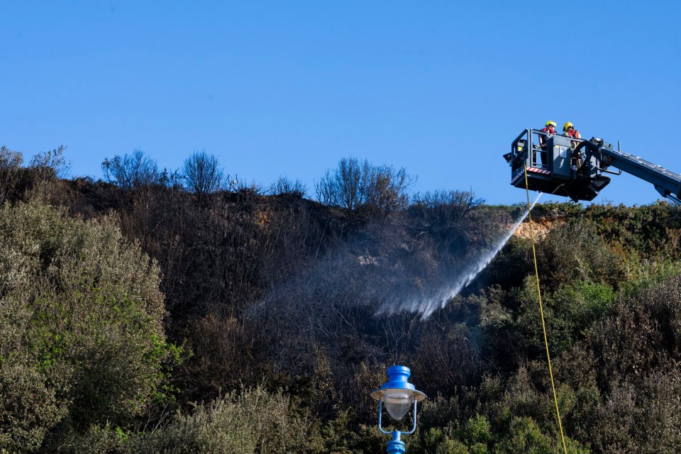 Los bomberos extinguiendo un incendio forestal en un acantilado.