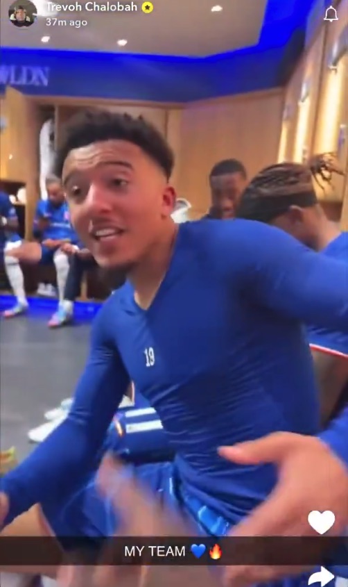 Jugador de fútbol con uniforme azul con compañeros de equipo en el vestuario.