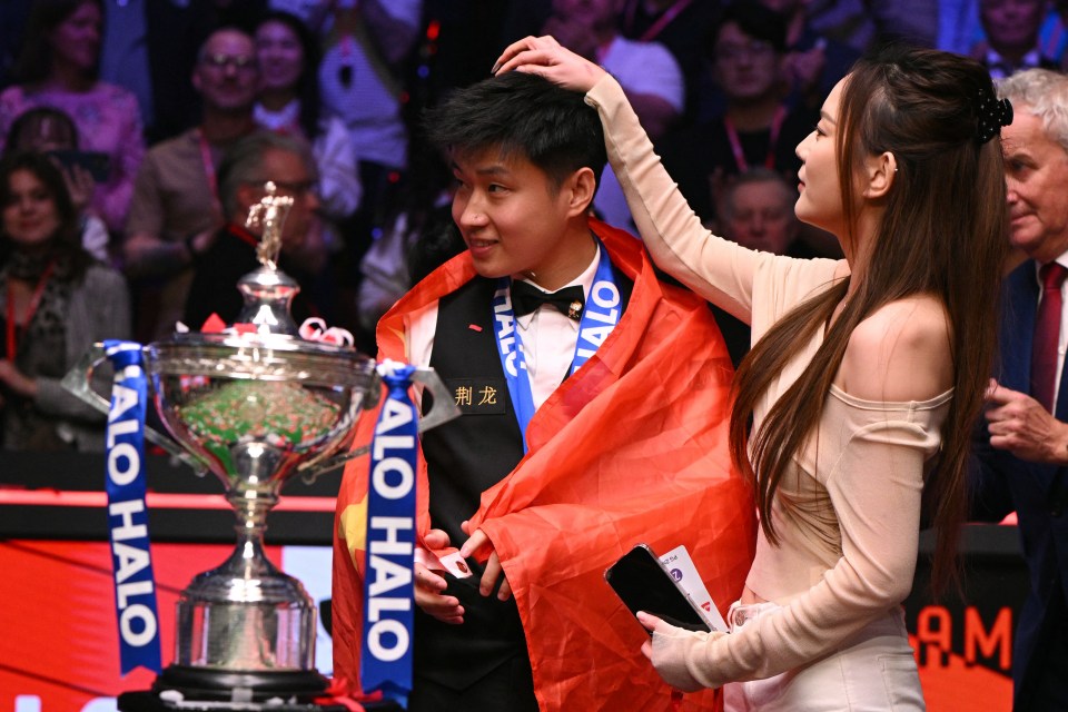 Zhao Xintong, el primer ganador del campeonato mundial de billar chino, con su novia y trofeo.