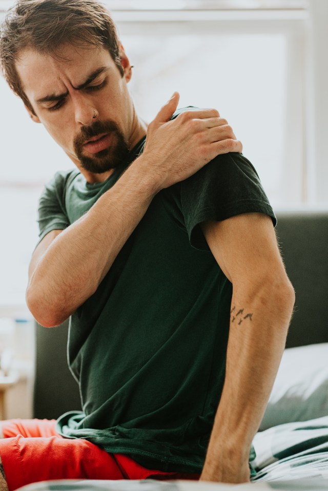 El hombre muuele de dolor mientras se frota el hombro.