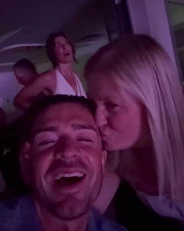 Un hombre riendo mientras una mujer besa su mejilla.
