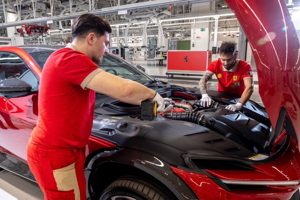 Dos trabajadores con camisas rojas de Ferrari que trabajan en el motor de un Ferrari rojo.