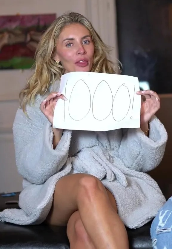 Mujer en una bata que sostiene un letrero que dice "1000!"