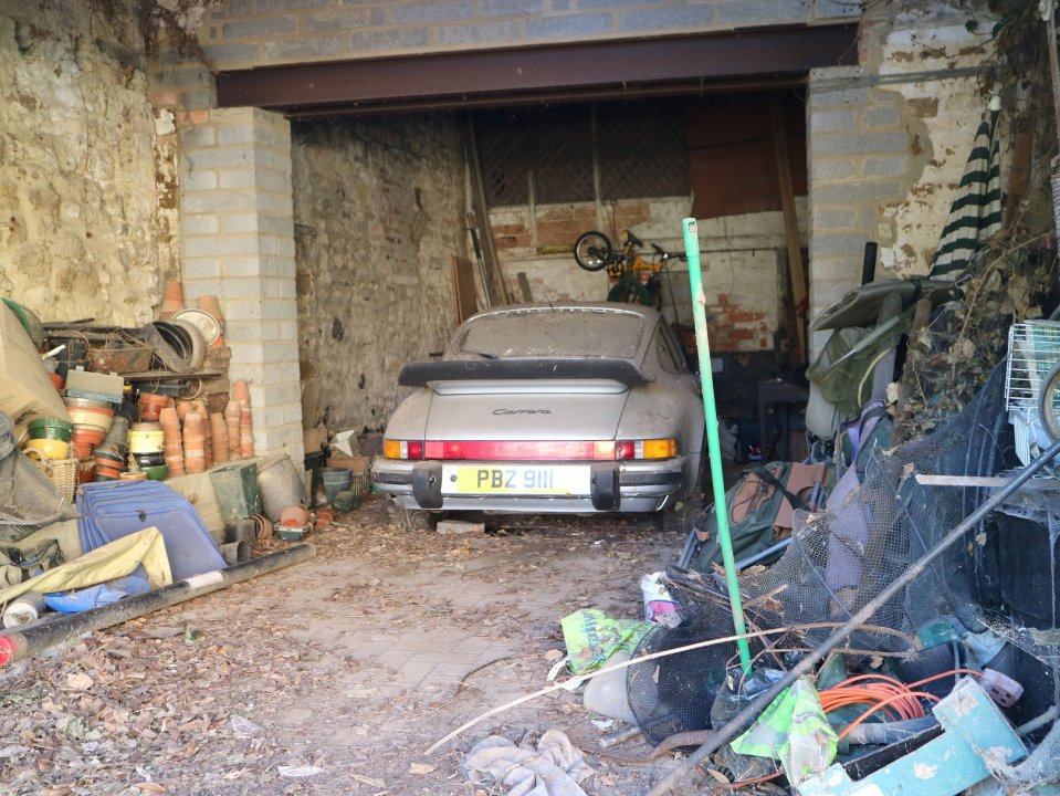 El polvoriento plateado Porsche 911 Carrera en un garaje desordenado.
