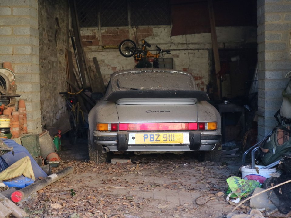 Dusty Porsche 911 Carrera en un garaje desordenado.