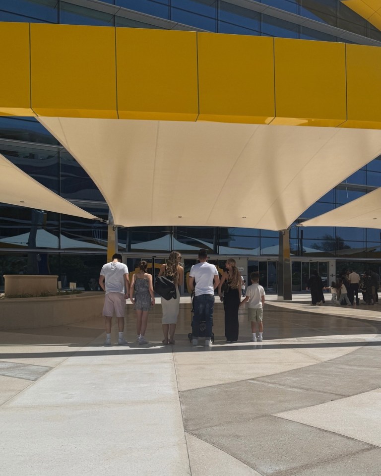 Familia de pie al aire libre bajo un toldo amarillo.