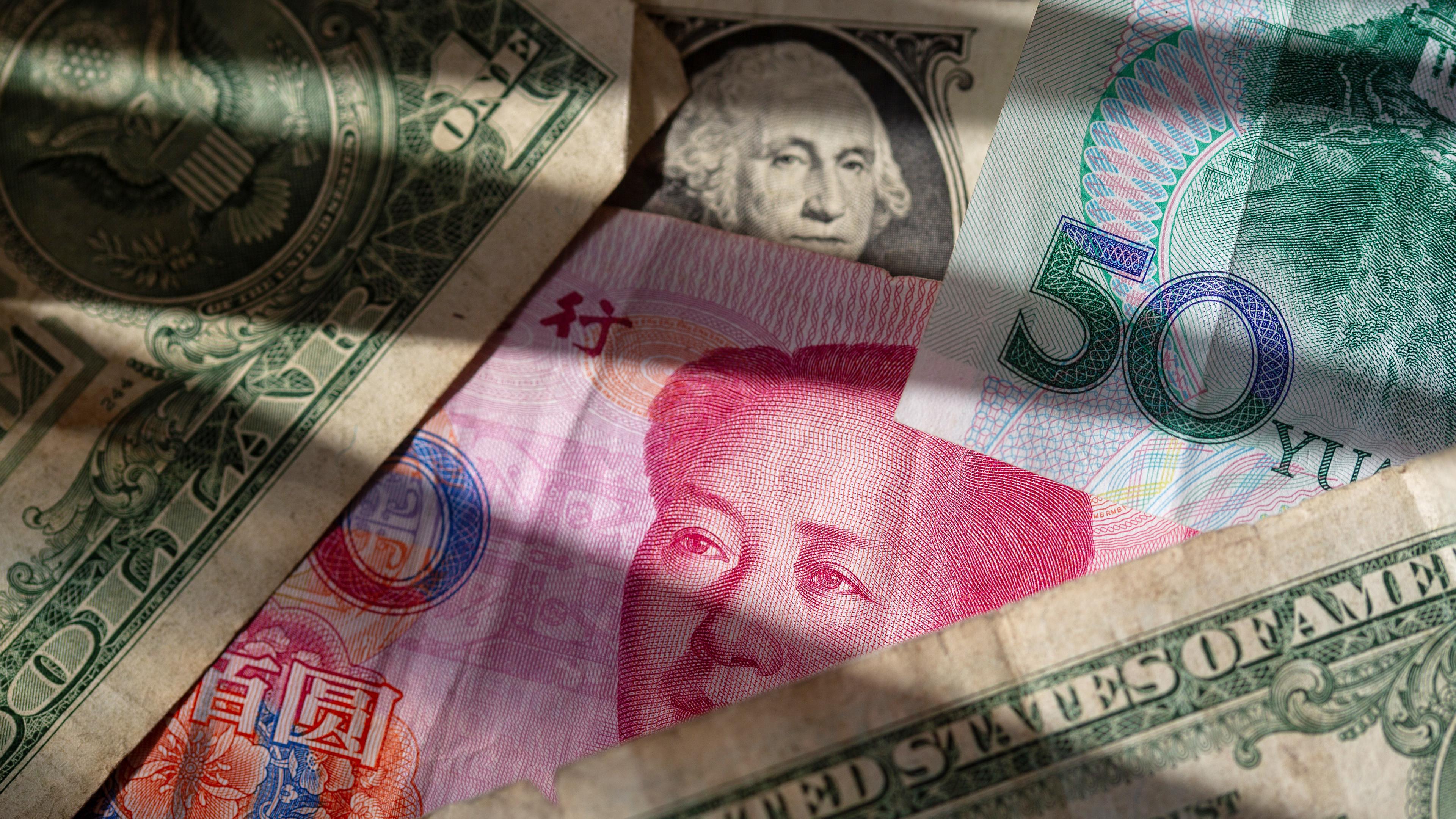 Los billetes yuanes chinos se encuentran entre varios signos de dólar estadounidense.