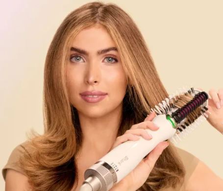 Mujer que usa un cepillo de estilo caliente en su largo cabello.