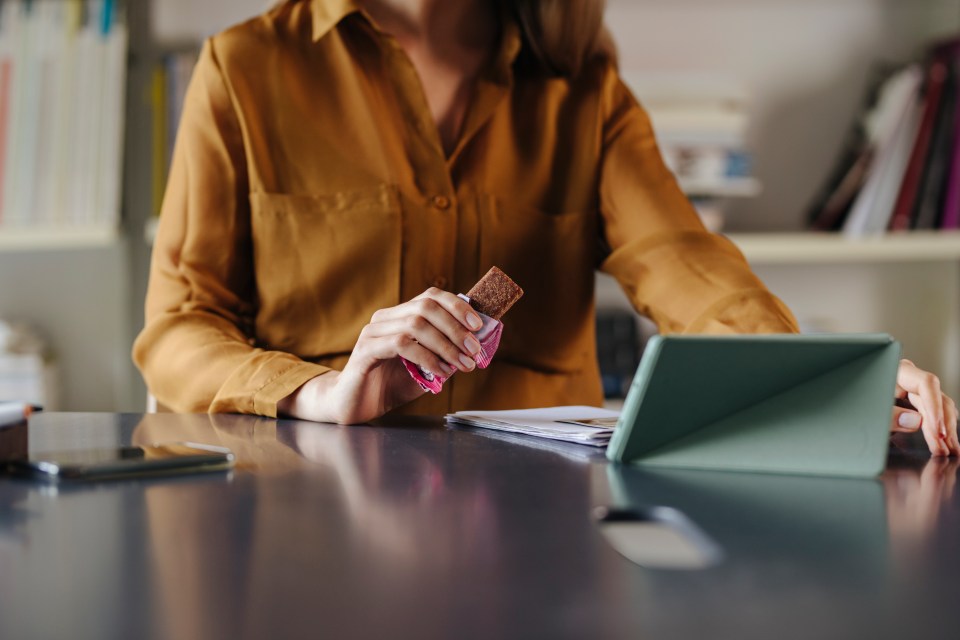 La empresaria come una barra de proteínas mientras trabaja en una tableta.