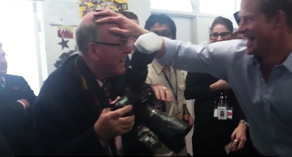 El príncipe Harry colocando juguetonamente su mano sobre la cabeza de un fotógrafo.
