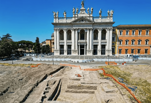 Ruinas excavadas de un antiguo palacio papal en Roma, frente a una basílica.