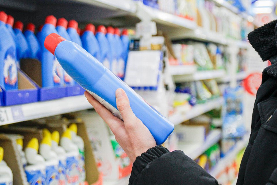 Persona que examina una botella de producto de limpieza azul en una tienda.