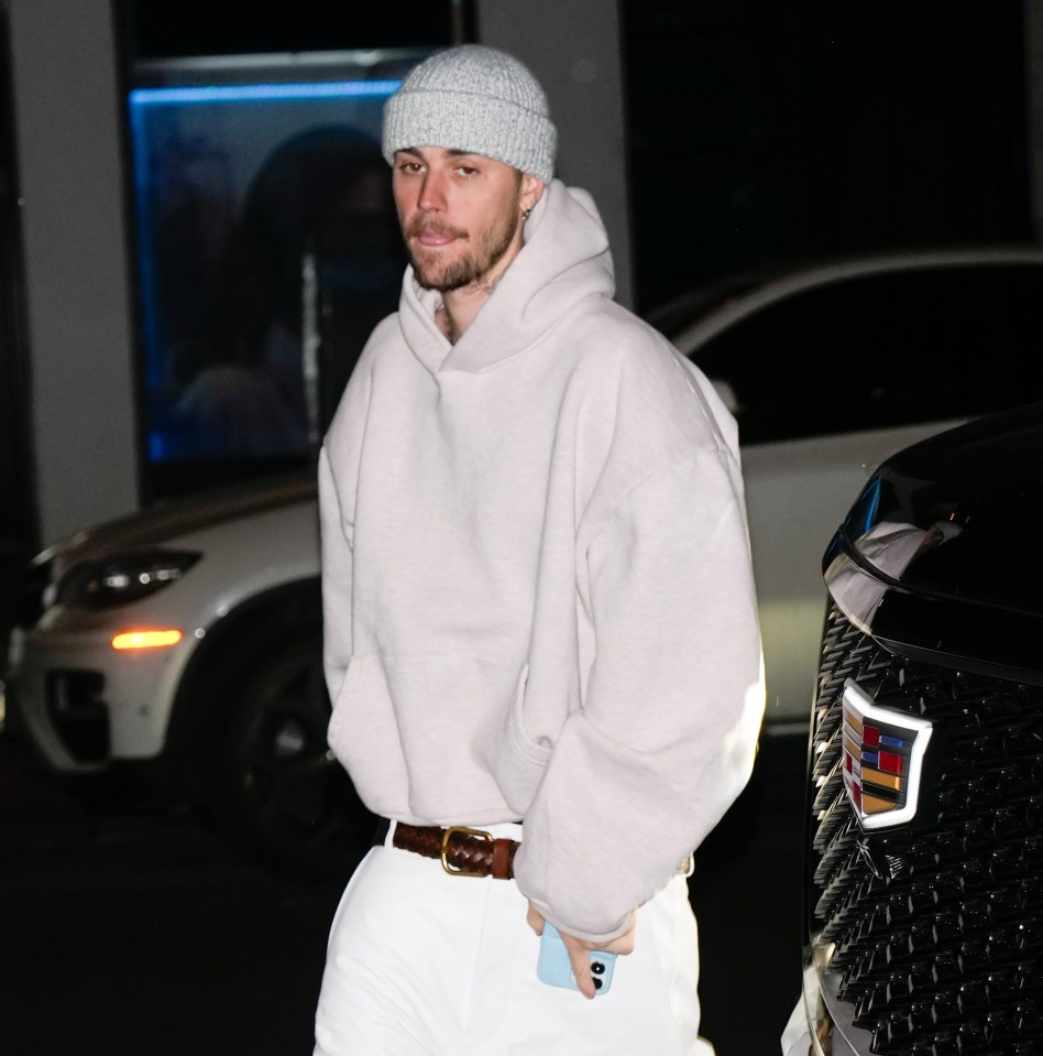 Justin Bieber con una sudadera con capucha de color claro, sombrero de punto y pantalones blancos.