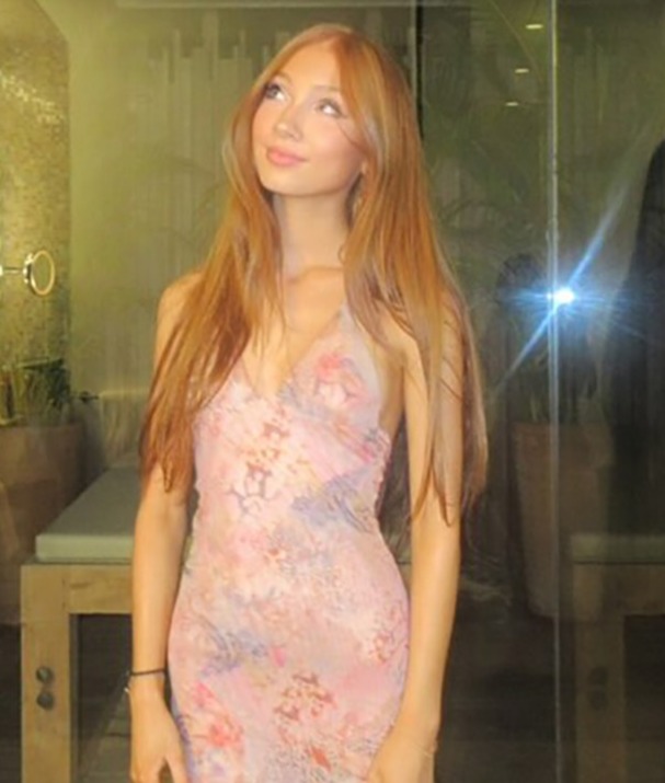 Mujer con vestido rosa frente a una pared de vidrio.