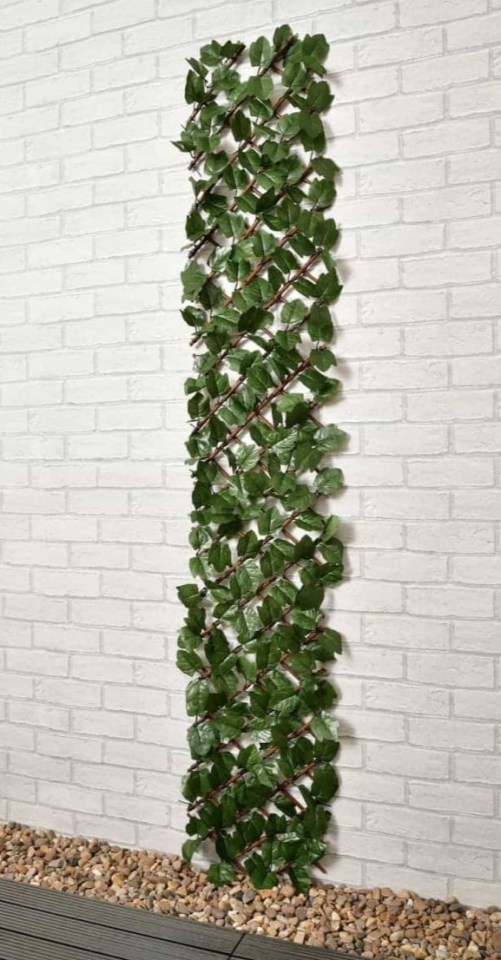 Trellis de hojas de hiedra artificial contra una pared de ladrillo.