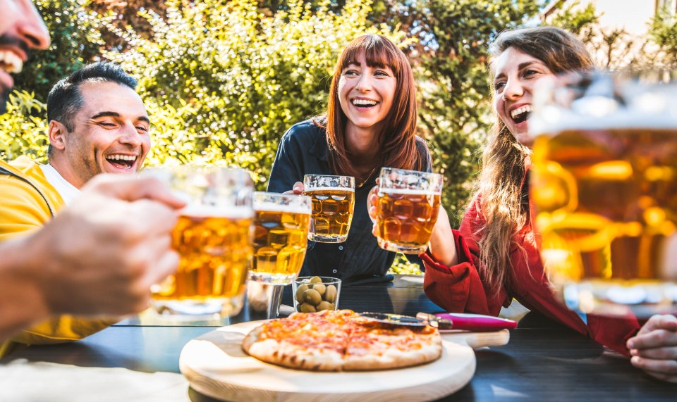 Grupo de adultos jóvenes tostando la cerveza en un restaurante al aire libre.
