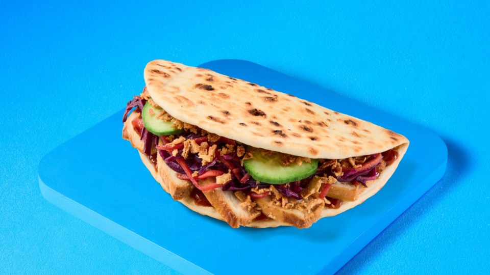 Sándwich de pan plano con repollo rojo, pepino y cebollas fritas.