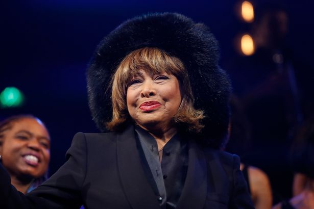 Tina Turner con un abrigo y sombrero oscuros se paró en un escenario.