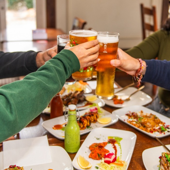Gente tostada con copas de cerveza en una mesa de restaurante con comida india.