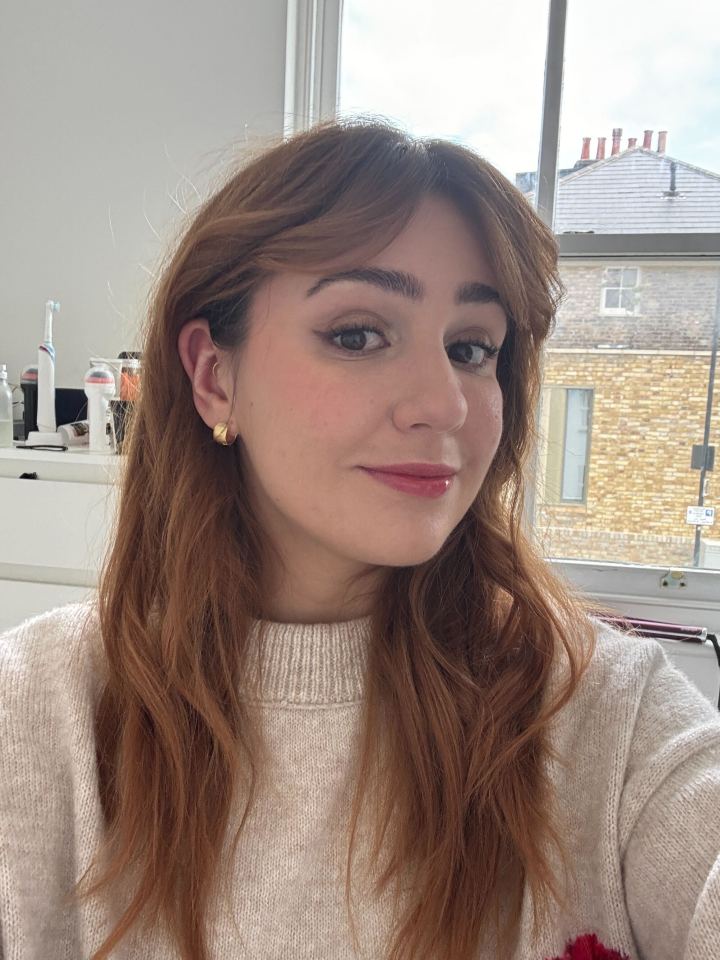 Mujer con cabello largo y castaño con un suéter beige.