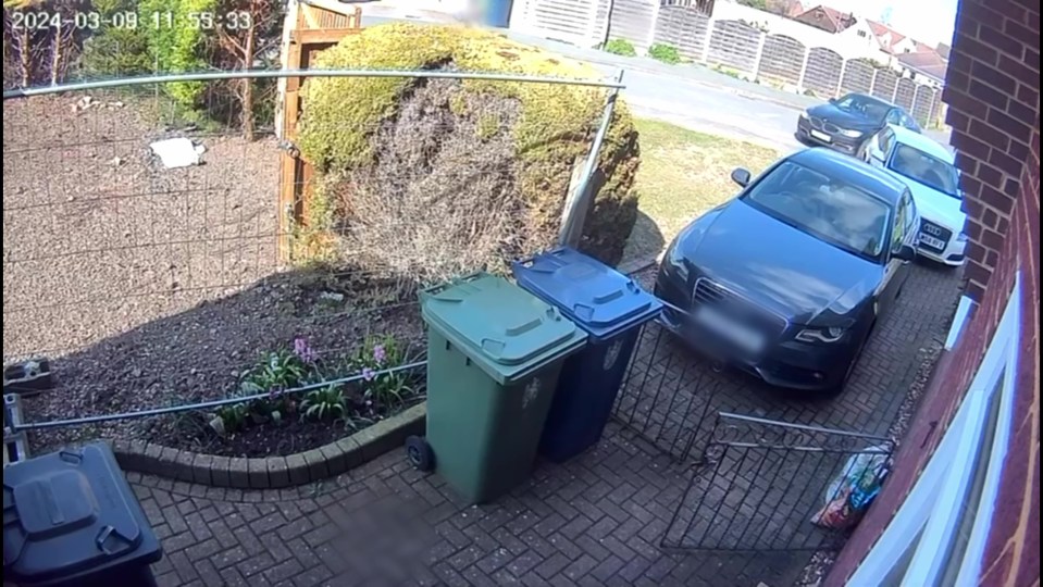 Imagen de CCTV que muestra un BMW de color oscuro que conduce hacia una mujer frente a una casa.