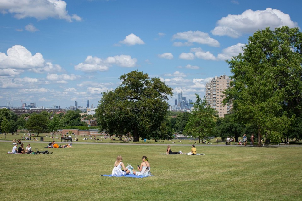 La gente disfruta de un día soleado en Brockwell Park, Londres, con el horizonte de la ciudad en el fondo.