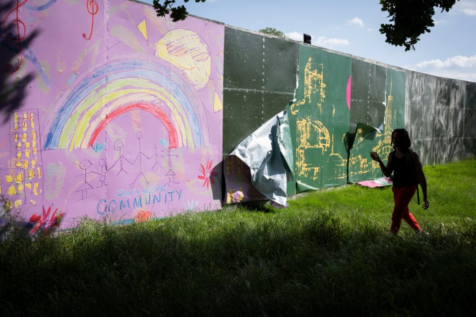 Persona que pasa junto a una pantalla de festival dañada con dibujos para niños.