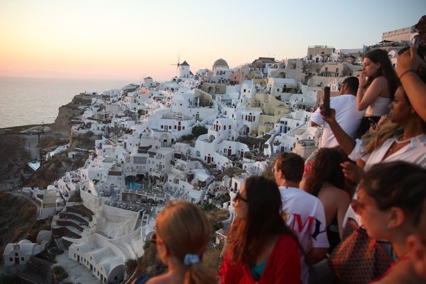 TOPSHOT - Los turistas esperan la puesta de sol en el pueblo de Oia en la isla griega de Santorini el 20 de julio de 2024. Al igual que otros destinos turísticos populares, la isla cicladic encaramada en un volcán se acerca a la saturación excesiva, y ahora quiere restringir la cantidad de cruceros. (Foto de Aris Oikonomou / AFP) (Foto de Aris Oikonomou / AFP a través de Getty Images)