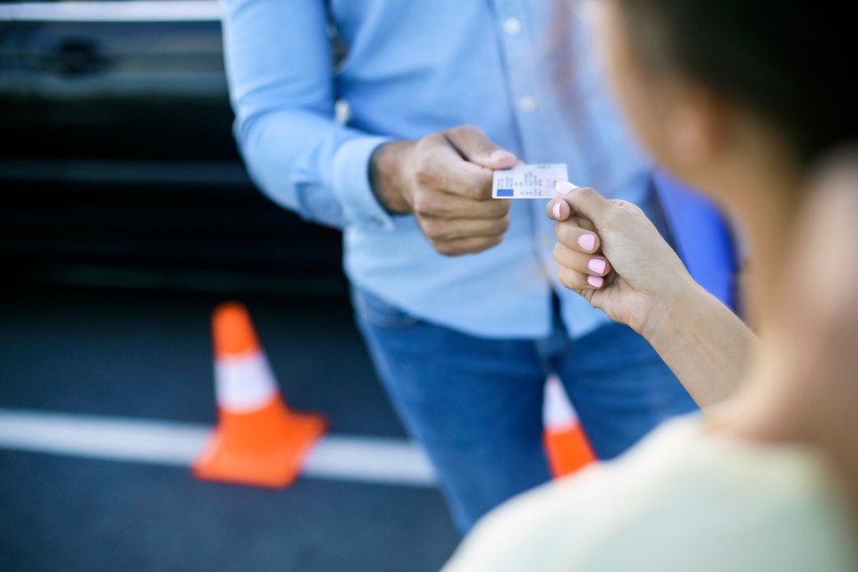 Instructor de conducir entregando a una mujer joven su licencia de conducir.
