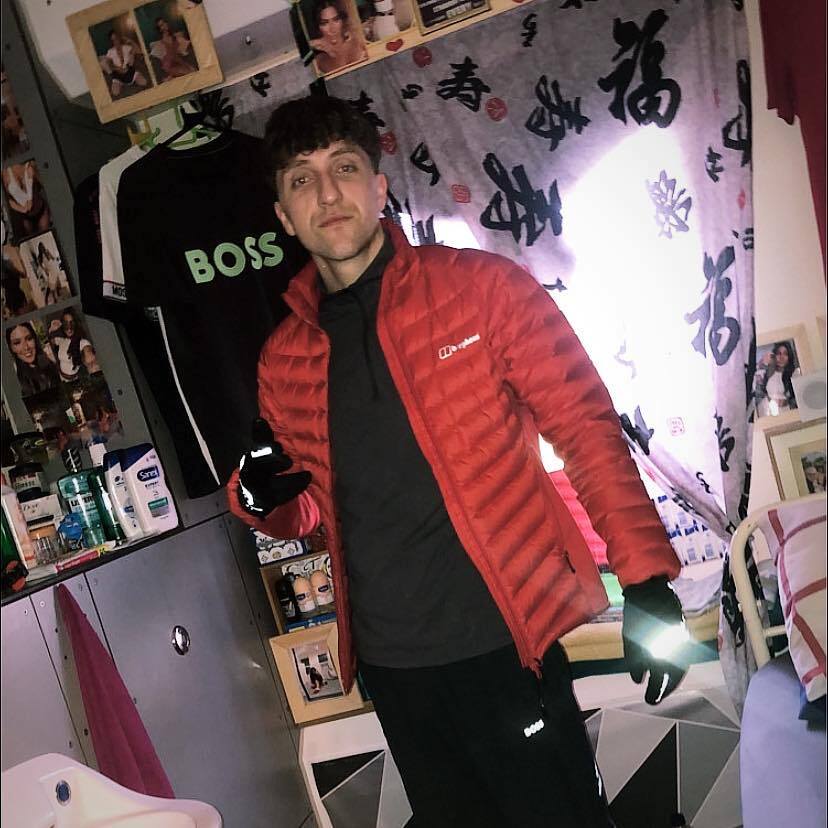 Un hombre con una chaqueta roja se encuentra en una celda de la prisión decorada con fotos.
