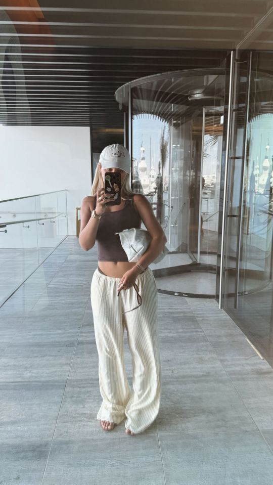Mujer tomando una selfie con una gorra blanca y pantalones rayados.