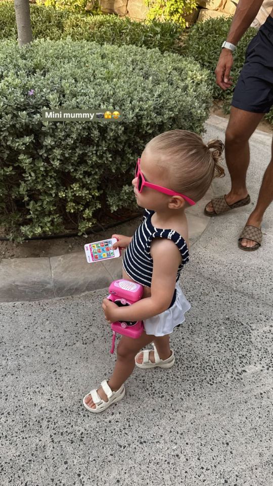 Chica para niños pequeños con gafas de sol y sosteniendo el teléfono y la cámara de juguete.