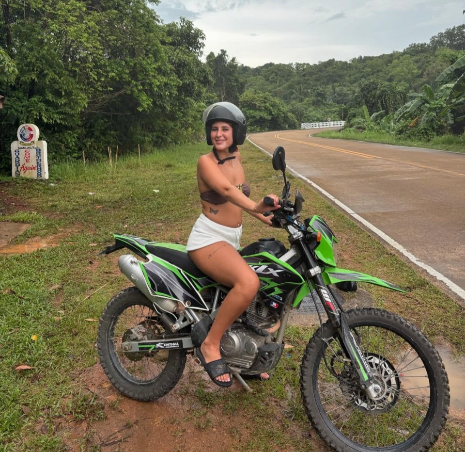 Una mujer joven sentada en una motocicleta verde en una carretera en Tailandia.