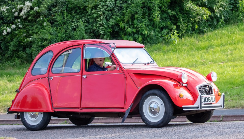 Un Citroën 2CV rojo de 1986 conduciendo por una carretera.
