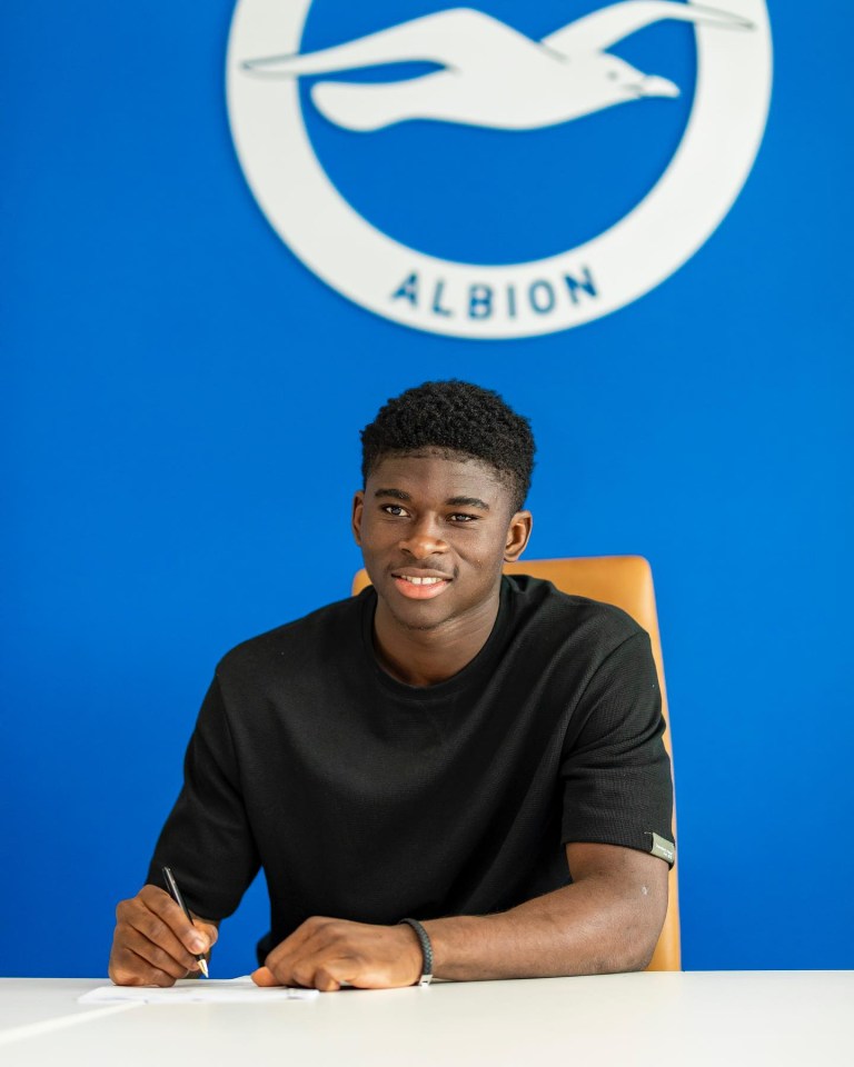 Un joven firmando un documento en una mesa, con el logotipo de Brighton & Hove Albion en el fondo.