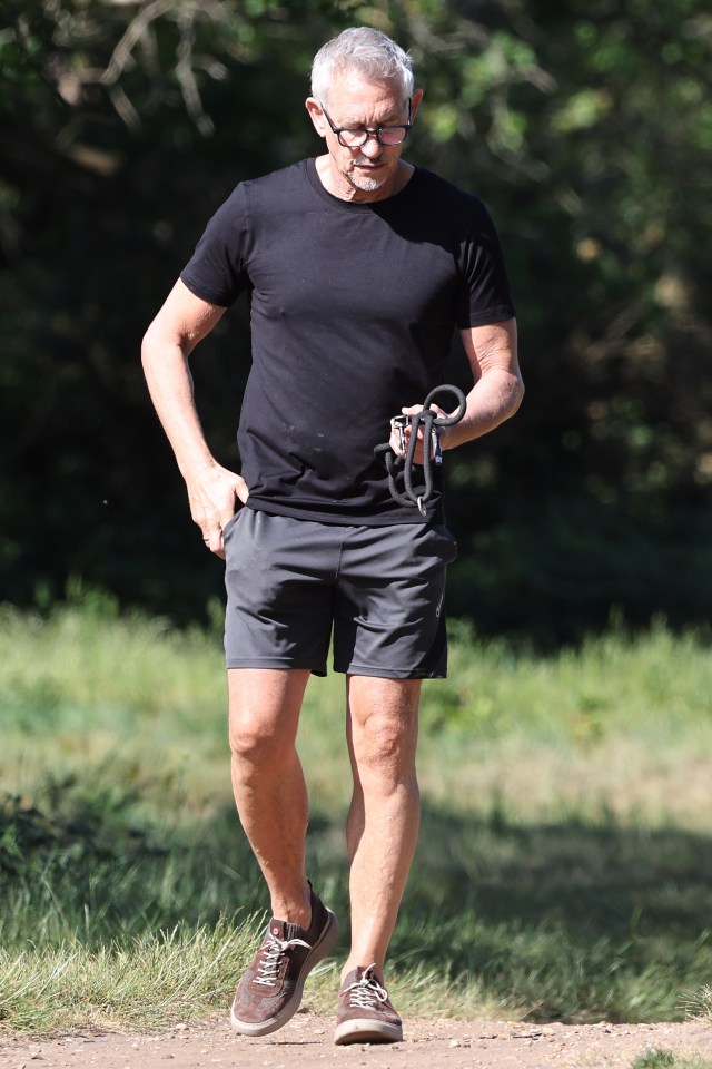 Gary Lineker caminando en un parque, sosteniendo una correa para perros.