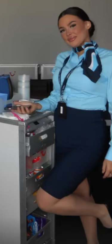 Asistente de vuelo en uniforme junto a un carrito de bebidas.