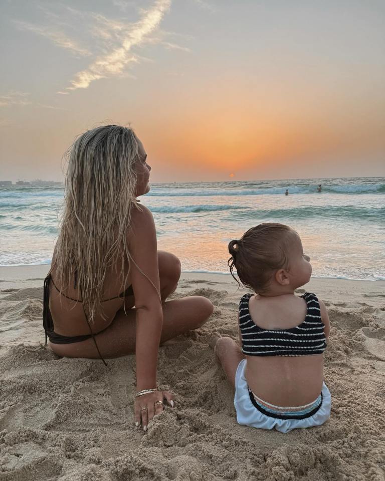 Mujer y niños pequeños sentados en la playa al atardecer.