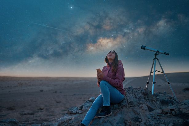 Mujer sentada en el desierto sola viendo el cielo estrellado y la Vía Láctea de fondo