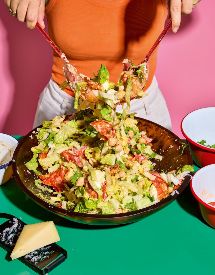Persona arroja una ensalada picada con salami y garbanzos.