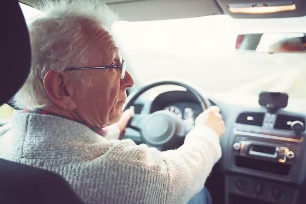 Viejo caballero amigable con gafas de marco de metal conduce coche